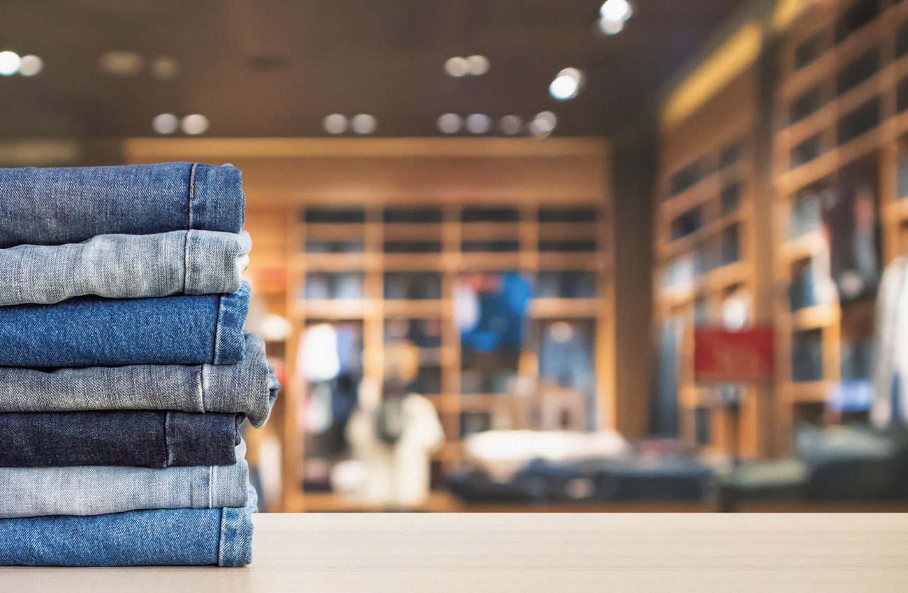 Blue denim jeans stack on wood table top with abstract blur clot